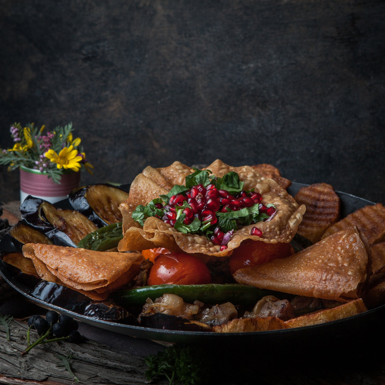 Close-up meat with baked potatoes, eggplant, tomato, pepper and decorated with pomegranate on wooden bark