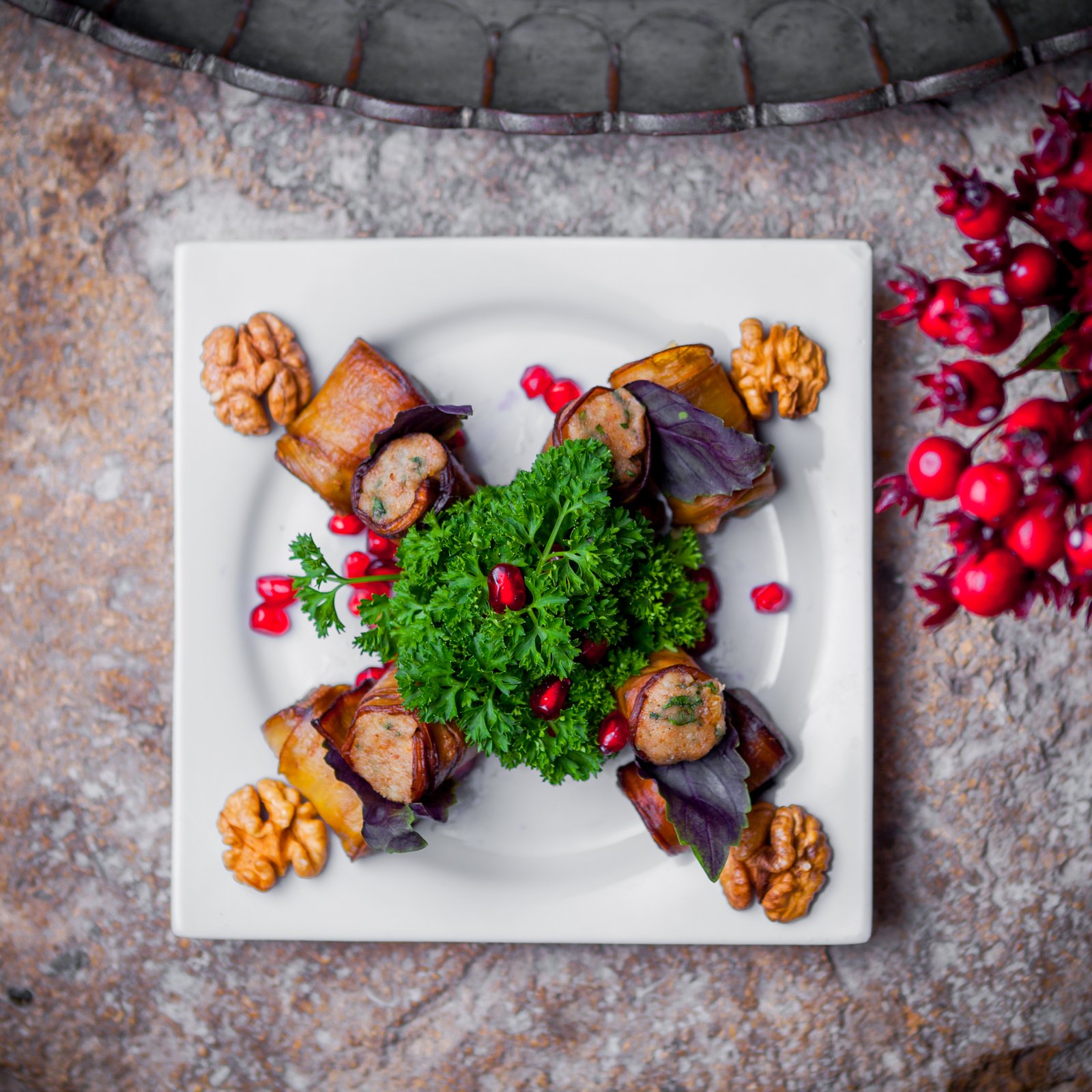 Top view salad eggplant rolls with pomegranate seeds and greens in white plate on stone background
